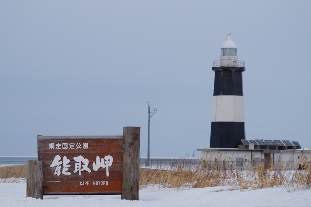 Lighthouse and sign stand in a snowy landscape.
